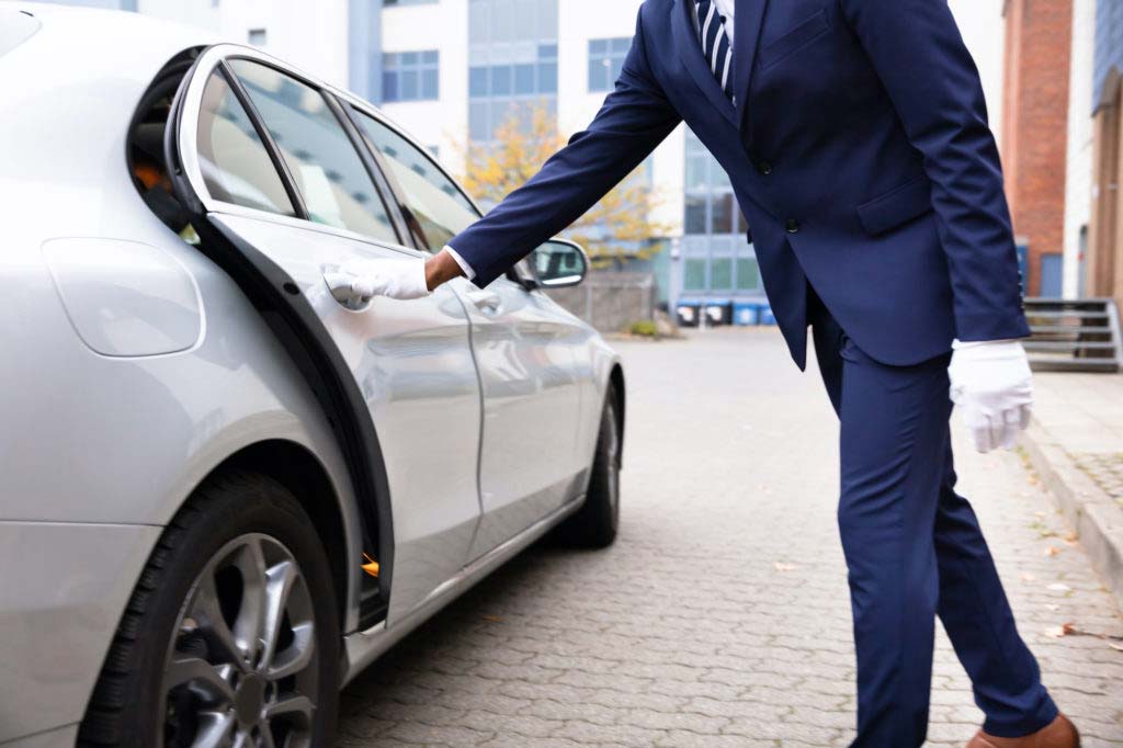 A concierge wearing gloves while opening a car door